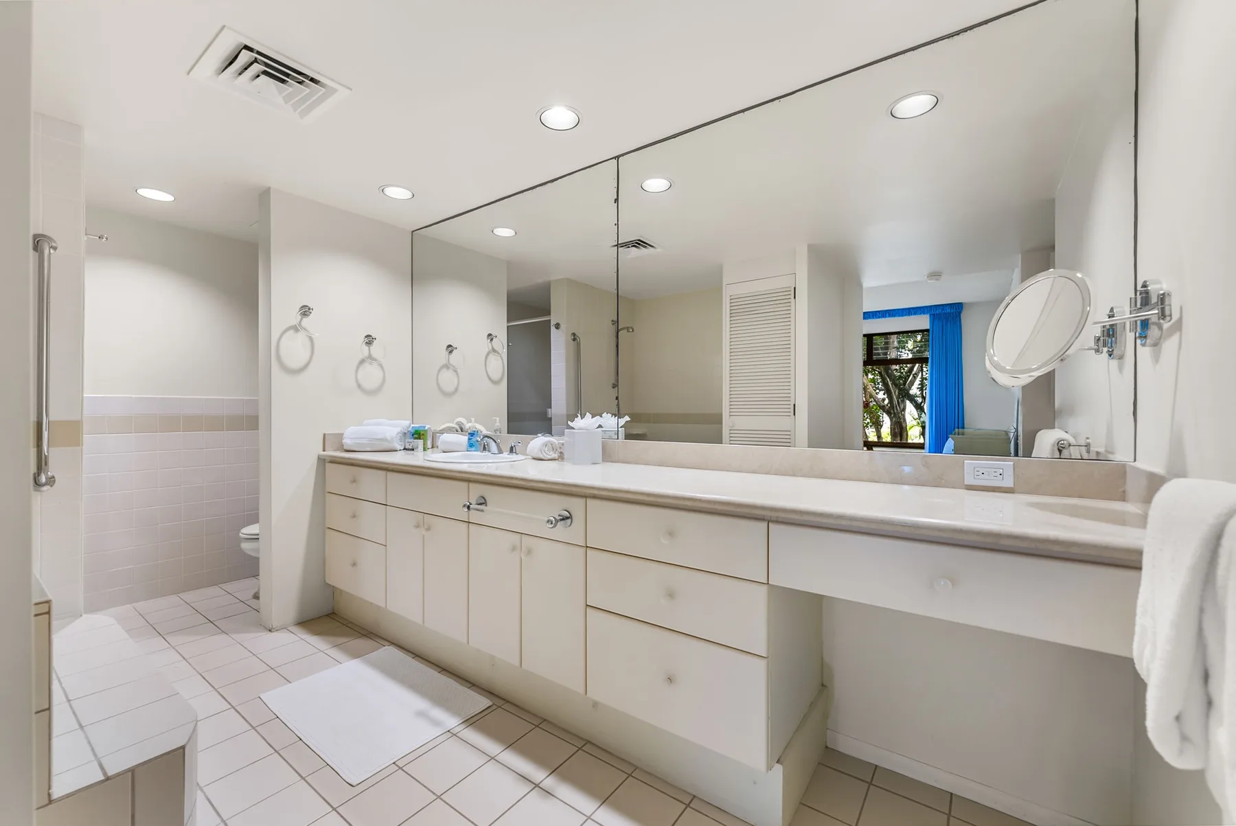 A bright bathroom with a long vanity, broad mirror, and tiled floor.