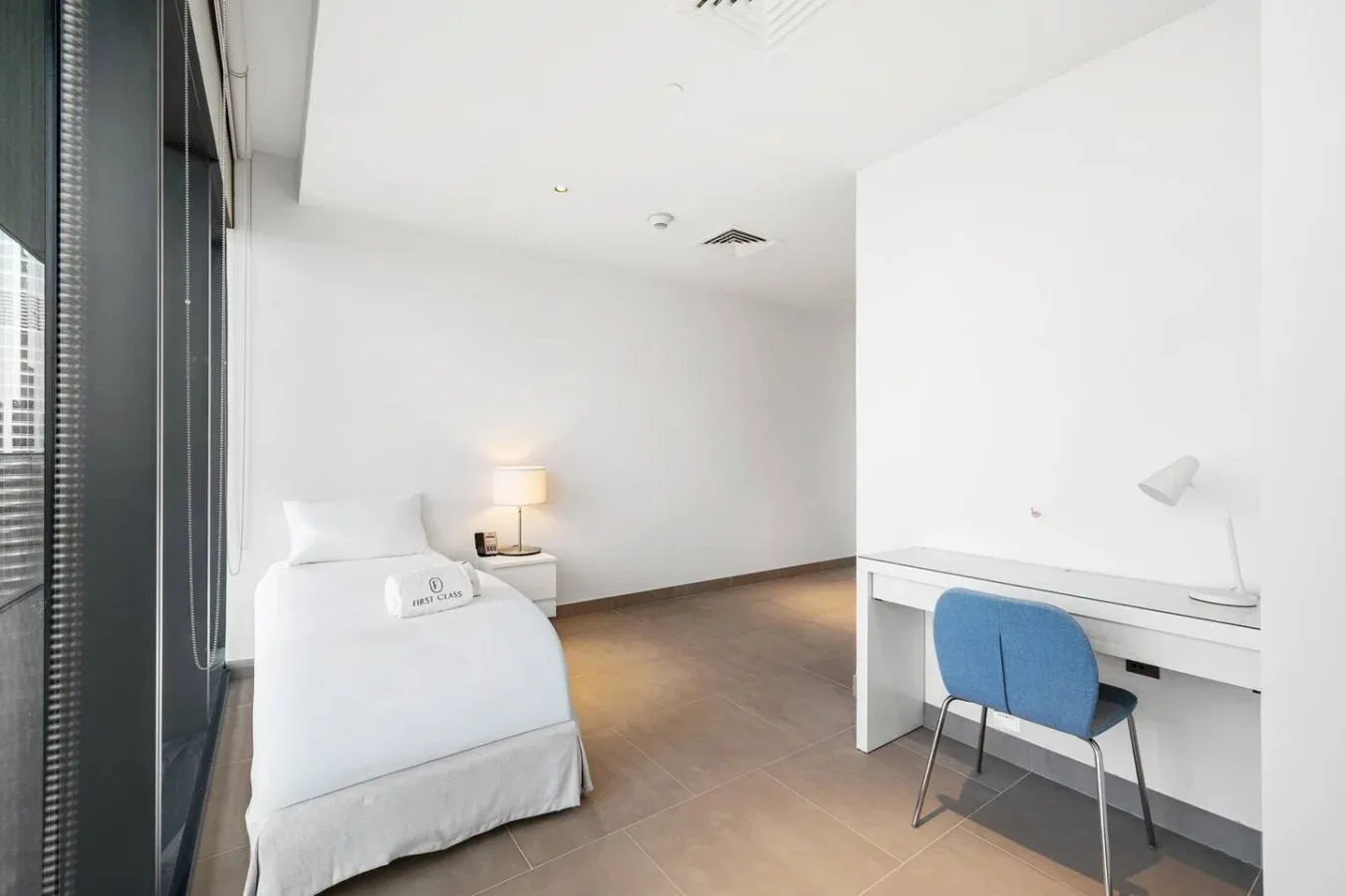Un dormitorio luminoso con una cama junto a un escritorio y una silla azul.