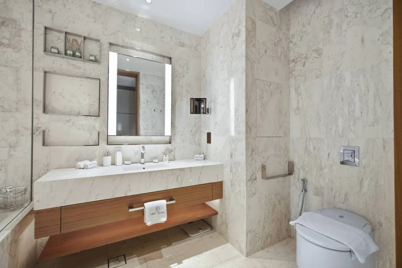Un baño revestido de mármol con tocador, espejo e inodoro.