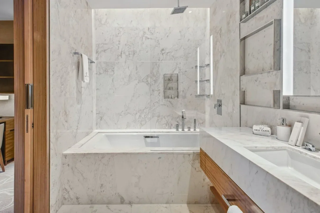 Un baño luminoso de mármol con bañera y un largo tocador.