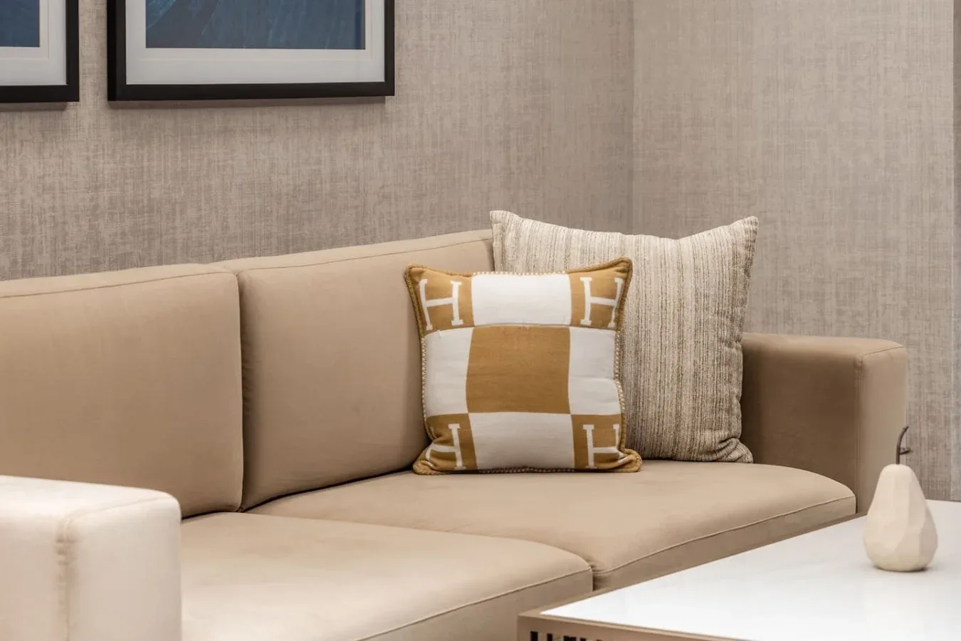 Una zona de estar beige con cojines estampados y cuadros enmarcados.
