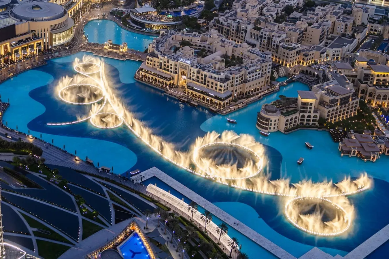 Vista aérea de fuentes iluminadas que danzan en una gran piscina junto a edificios.