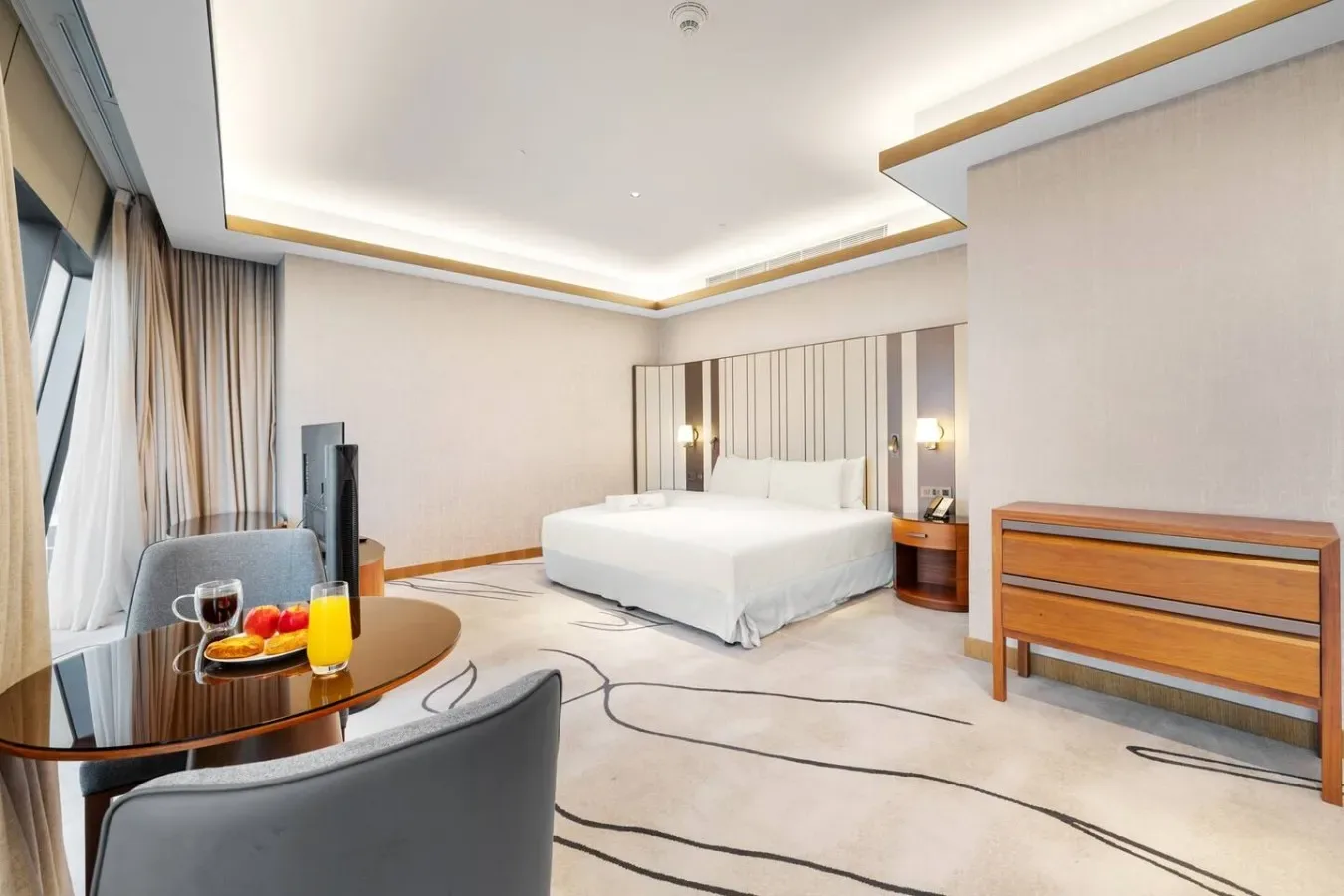 A bright bedroom with a bed, bedside tables, and a round dining table by the window.