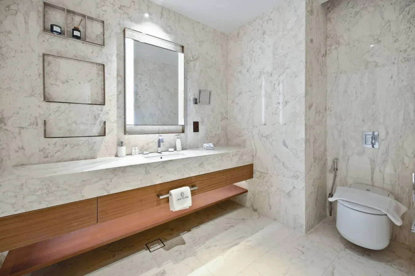 Un baño de mármol con un tocador largo, espejo e inodoro.
