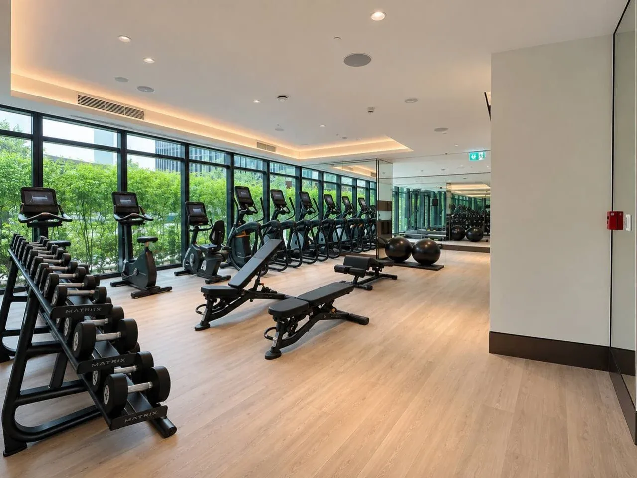 Un gimnasio con máquinas de ejercicio, bancos de pesas y grandes ventanas.