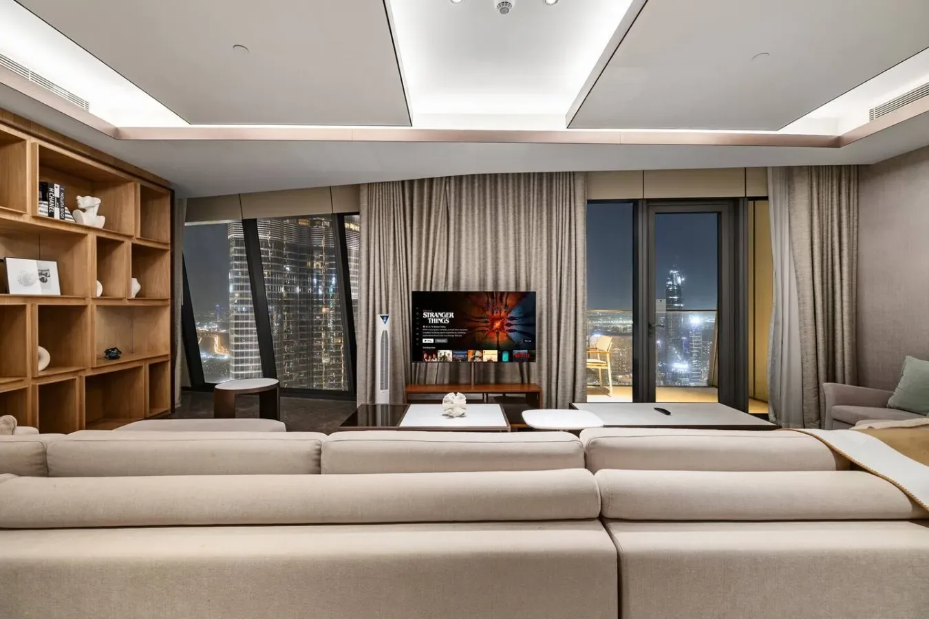 Una sala de estar moderna con asientos, televisor y grandes ventanas con cortinas.