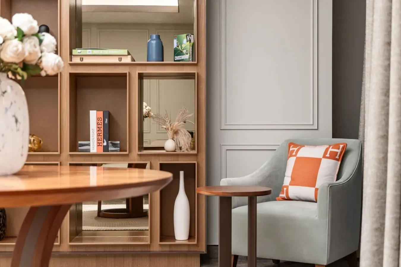 Una zona de estar con un sillón gris, mesitas y estanterías de madera.