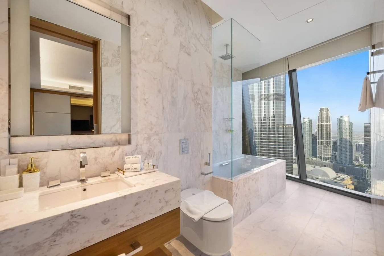 Un baño de mármol con ducha de vidrio y grandes ventanales con vistas a la ciudad.