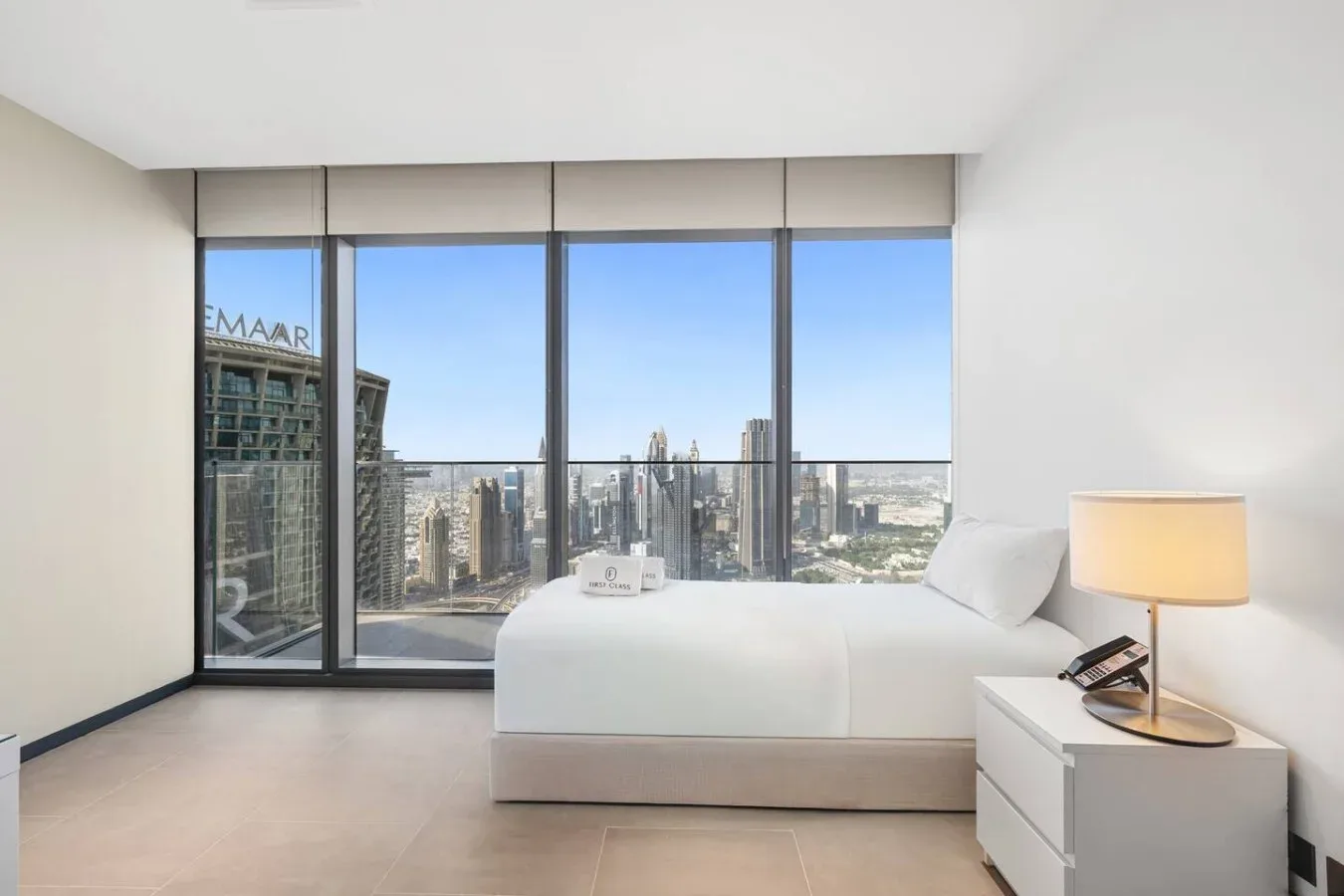 Un dormitorio con una cama blanca junto a ventanales con vistas a la ciudad.