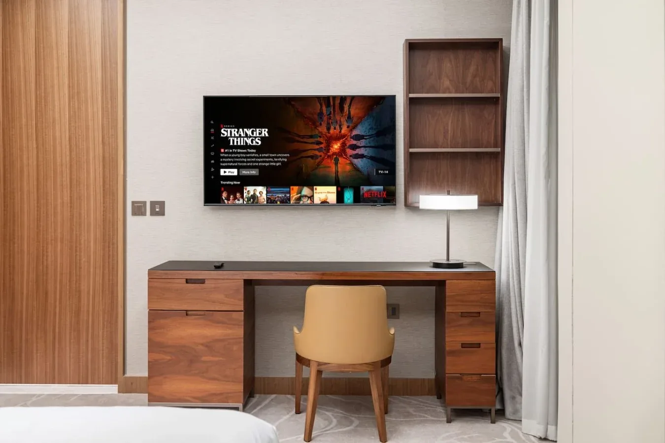 Un espacio de trabajo en un dormitorio con escritorio, silla, televisor y cortinas.