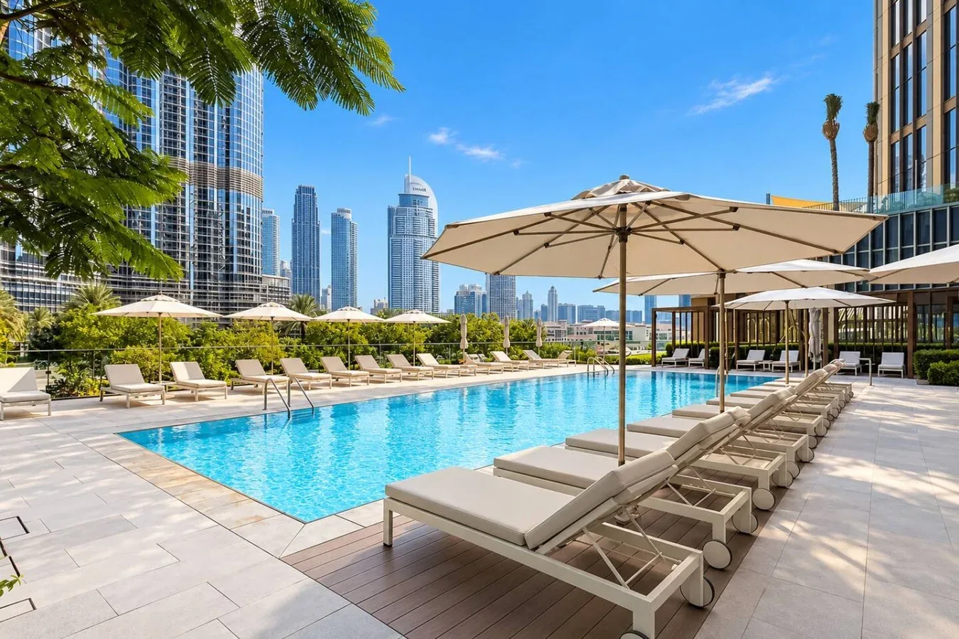 Una terraza de piscina al aire libre con asientos y sombrillas, rodeada de edificios urbanos.