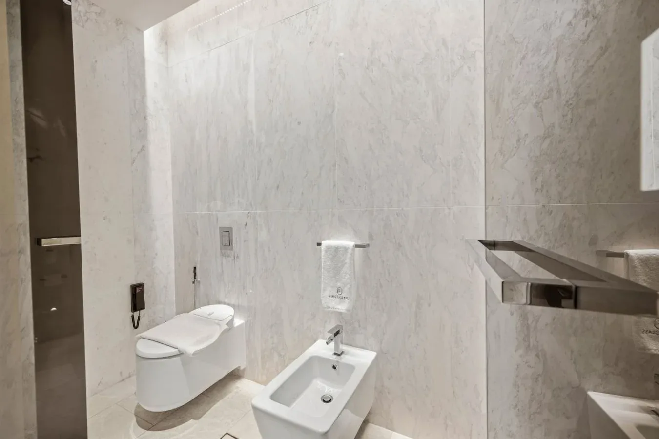 Un baño revestido de azulejos con inodoro, bidé y toalla colgada en la pared.