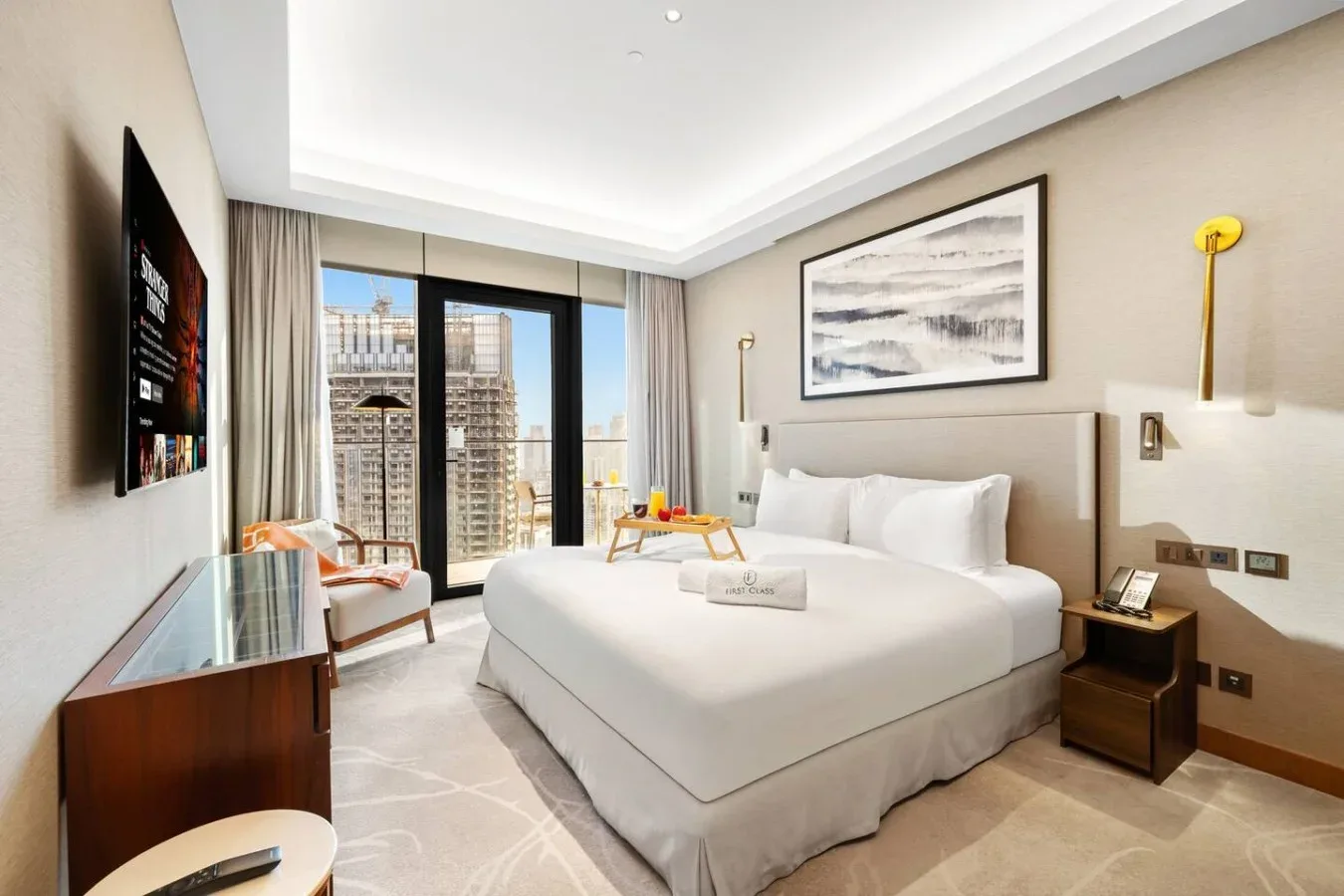 Un dormitorio con una cama grande, una mesita de noche y ventanas con vista a edificios cercanos.