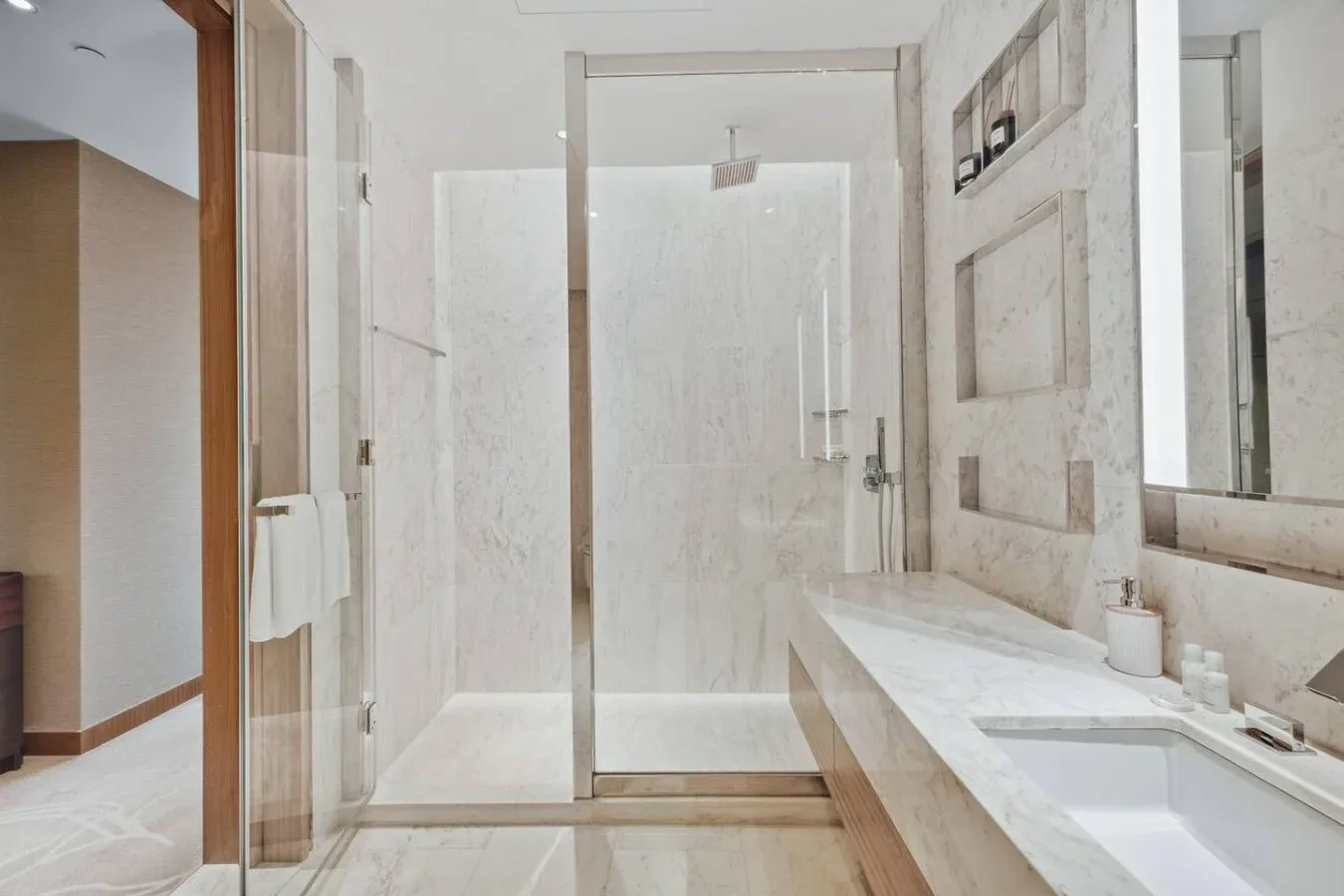 Un baño luminoso con ducha de vidrio y un tocador largo.