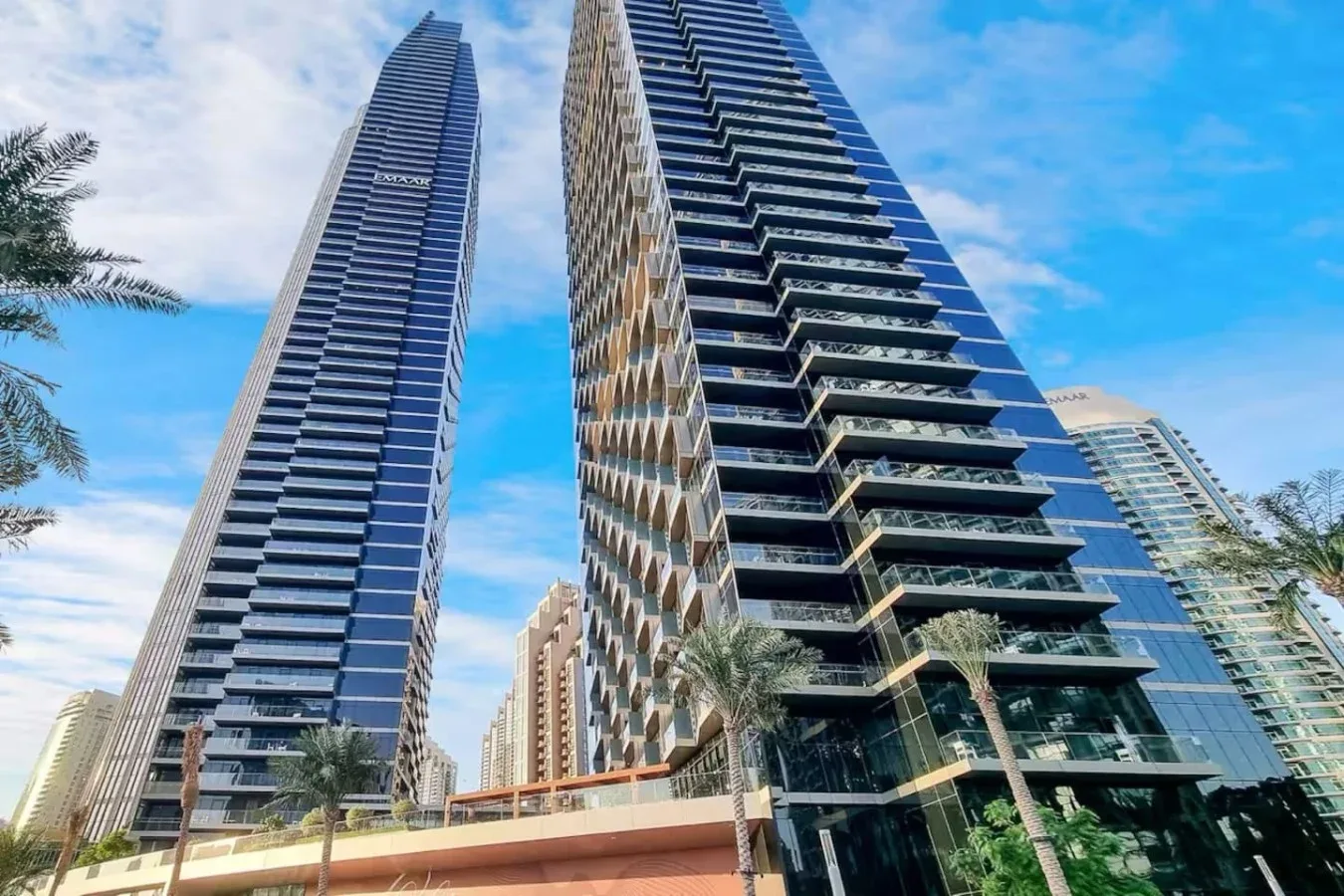 Edificios modernos de gran altura con balcones de vidrio se alzan sobre palmeras.