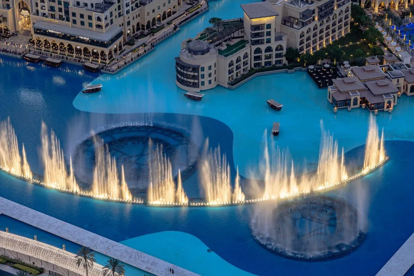 Vista aérea de una piscina turquesa con una línea curva de fuentes iluminadas.