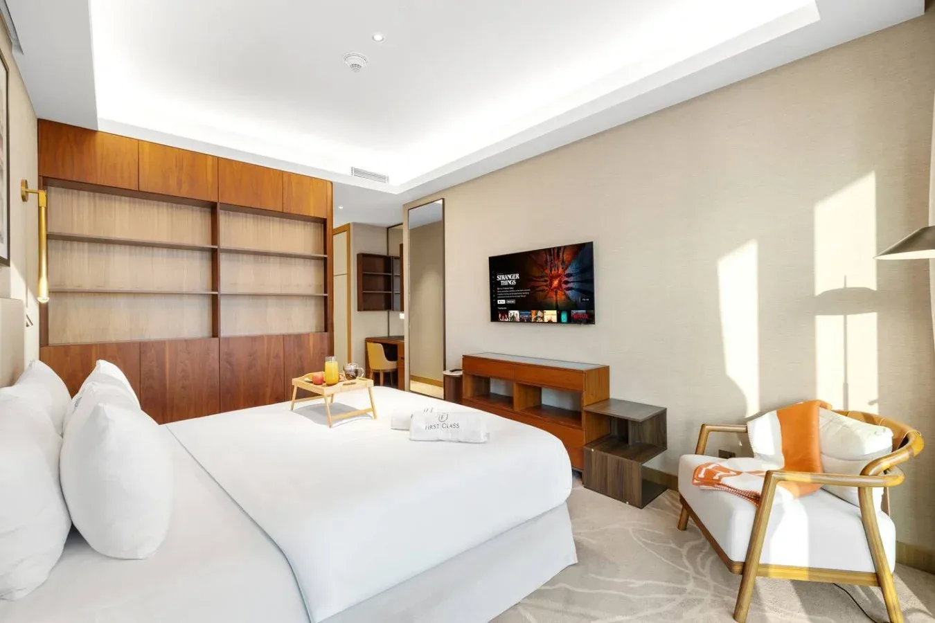 Un dormitorio luminoso con una cama, un televisor de pared y una zona de estar.
