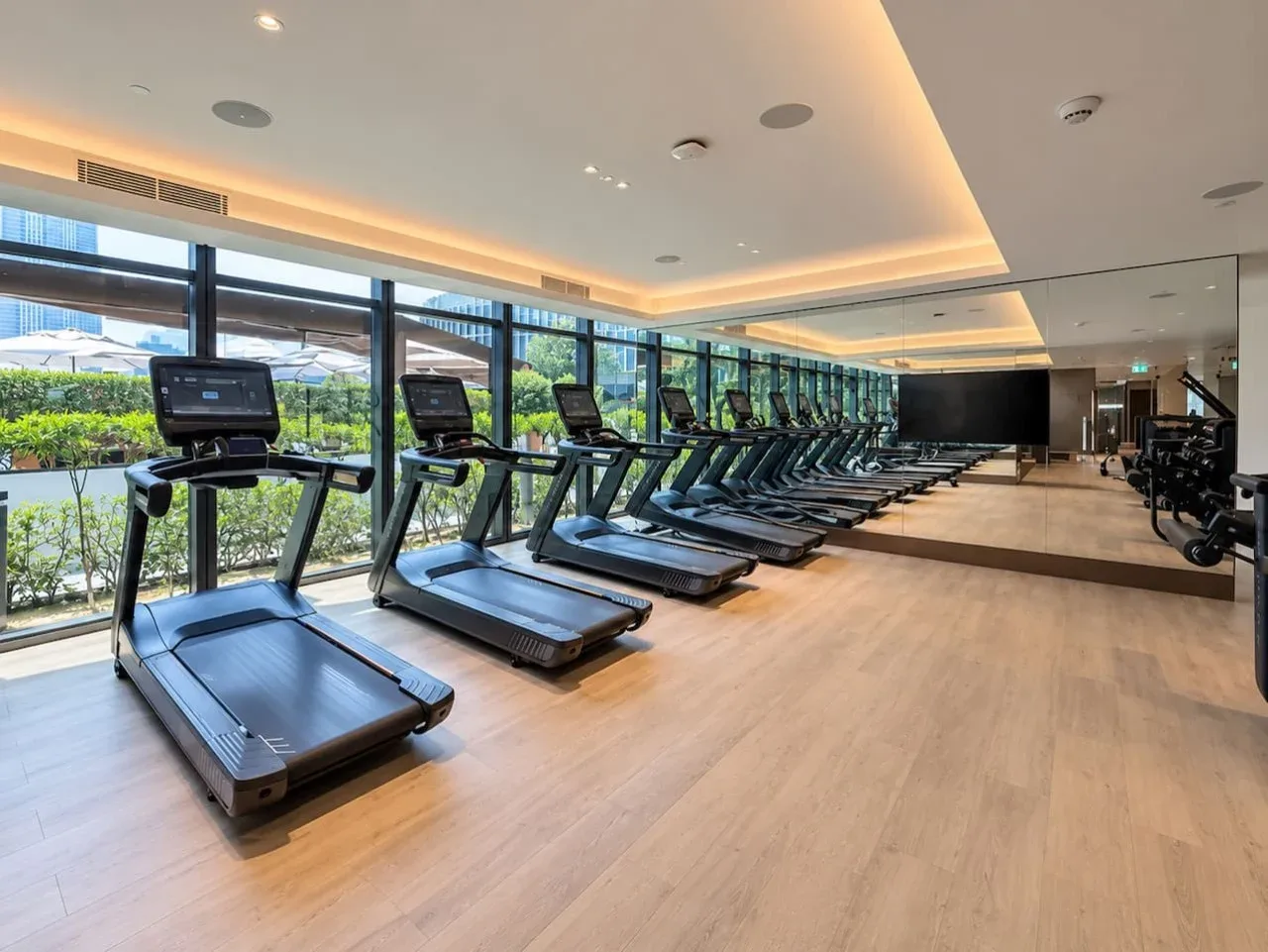 Un gimnasio con cintas de correr junto a grandes ventanales.