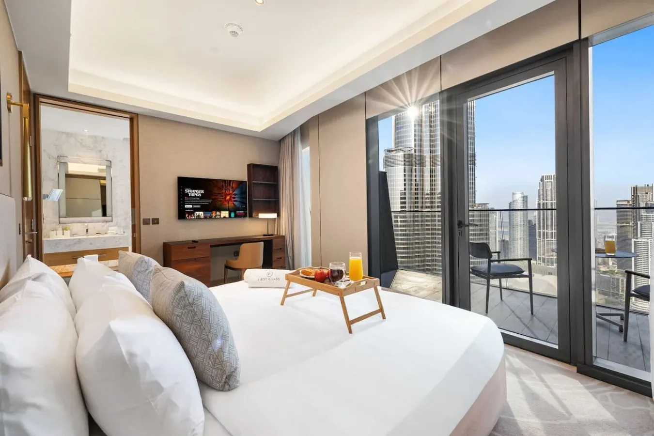 Un dormitorio con una cama, un escritorio y grandes ventanas con vistas a edificios de la ciudad.