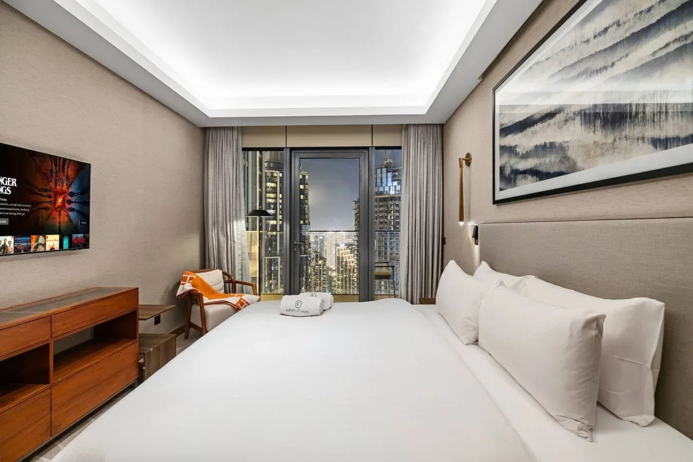 Un dormitorio con una cama grande, asientos y vistas de la ciudad a través de las ventanas.