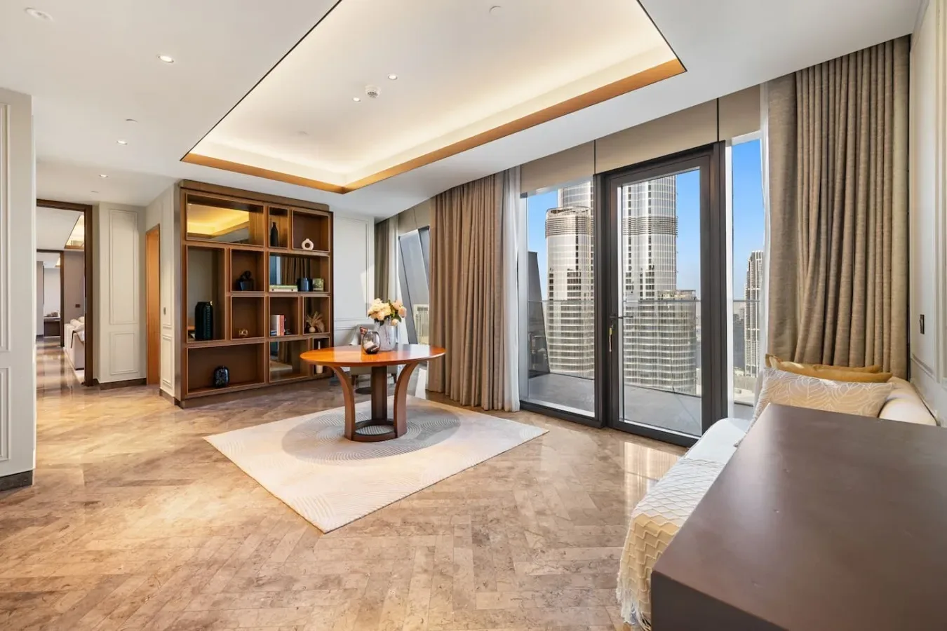 A bright living area with a round table, shelving, and floor-to-ceiling windows.