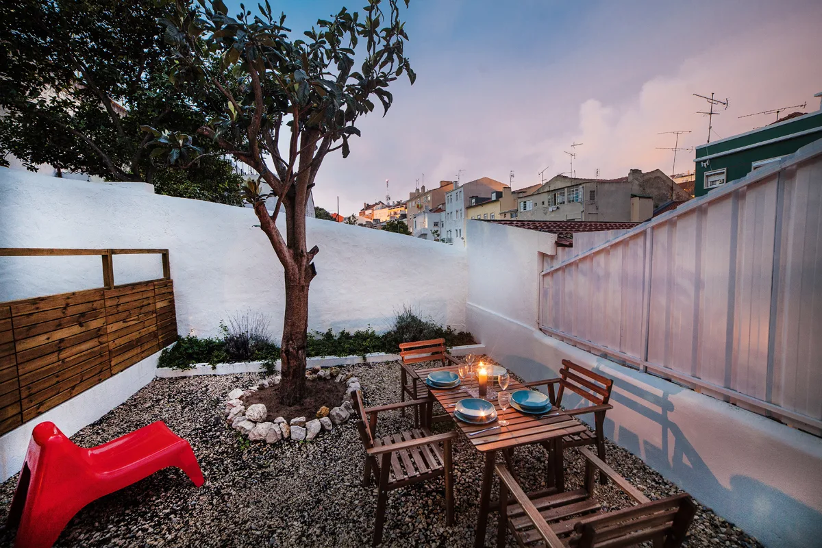 A small outdoor patio with a dining table, seating, and a tree.