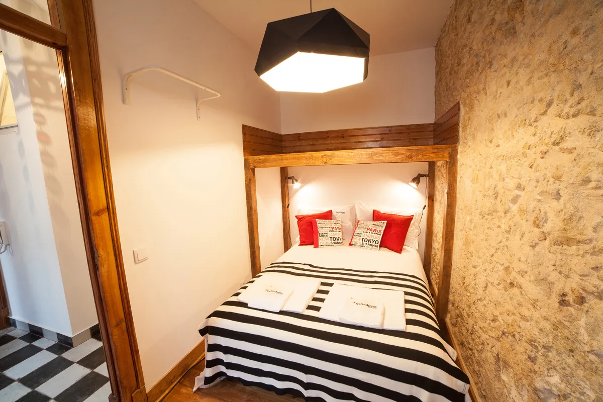 A bedroom with a striped bed beneath a wooden canopy.