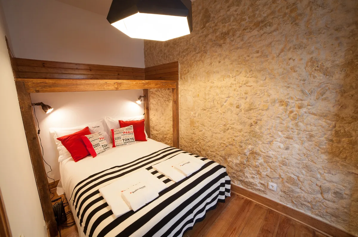A bedroom with a bed dressed in striped bedding beside a textured stone wall.