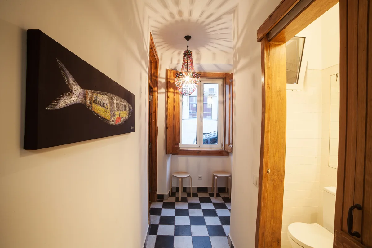 A narrow hallway with a black-and-white checkered floor and a window at the far end.