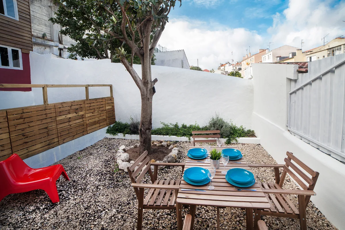 A gravel patio with wooden outdoor seating and a tree.