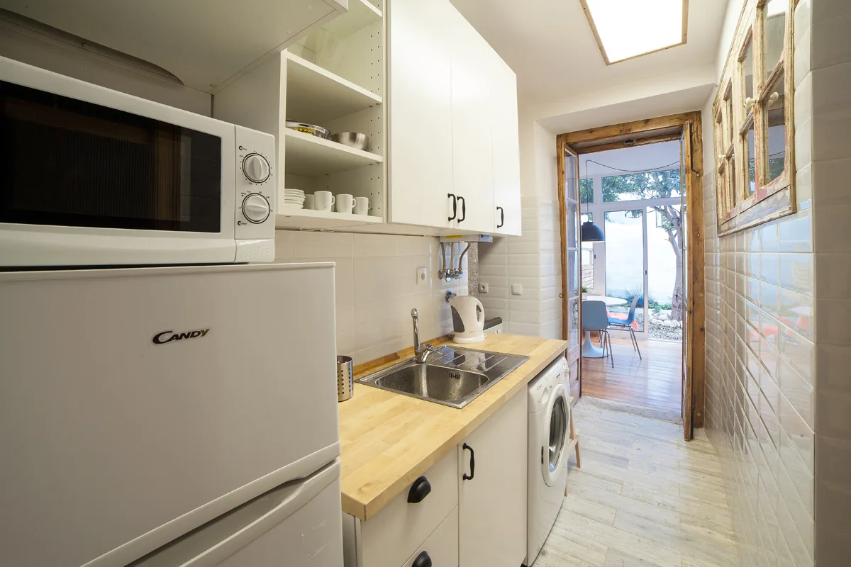A narrow kitchen with a countertop, sink, and appliances beside an open doorway.