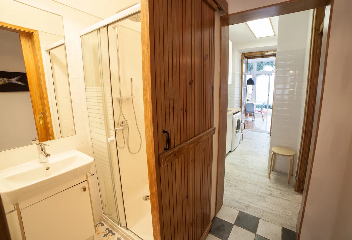 A bathroom with a sink and shower opens onto a bright adjoining room.