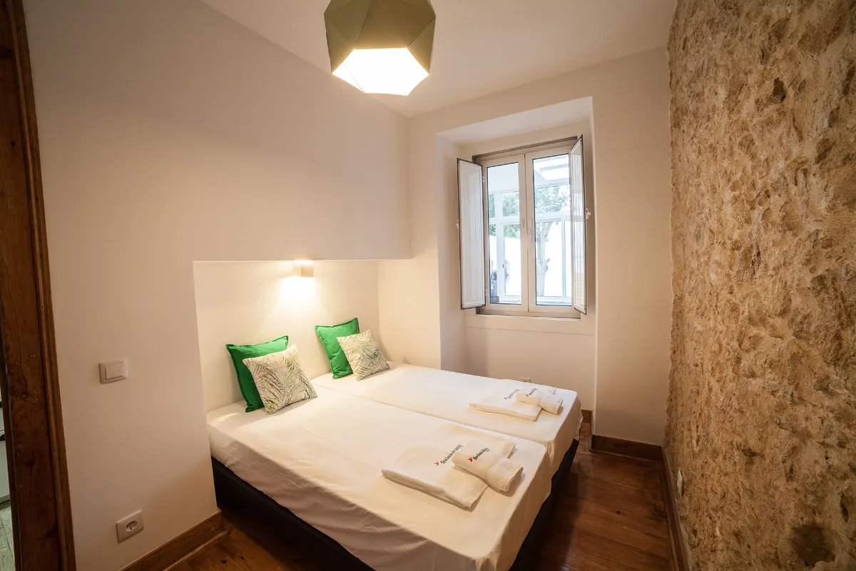 A bedroom with a double bed, green pillows, and a window.