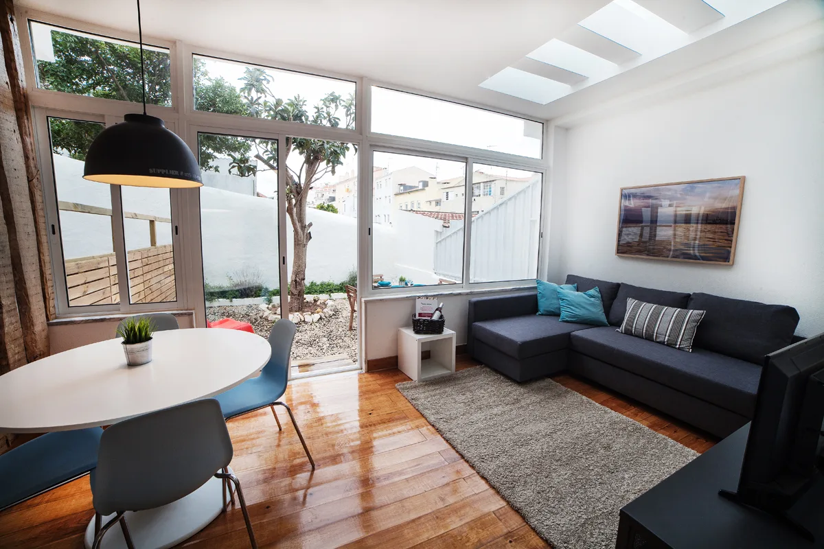 A bright living room with a dining table, seating, and large windows overlooking a patio.