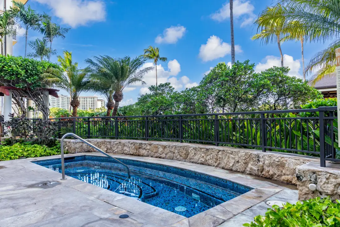 Una piscina al aire libre está rodeada de vegetación tropical y un muro de piedra.