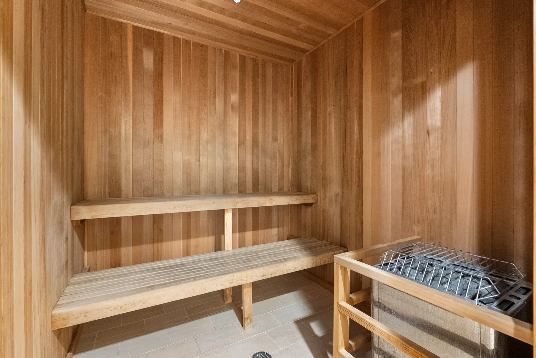 Una sauna revestida de madera con asientos escalonados y un calefactor.