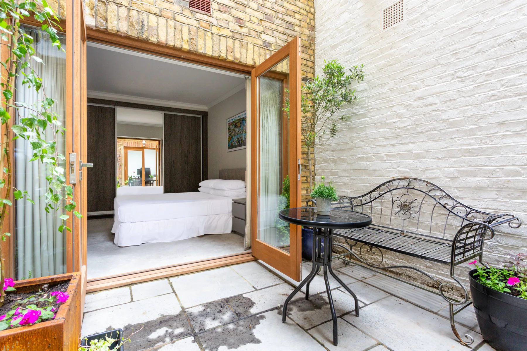 A bedroom opens onto a small stone patio with a metal bench and table.