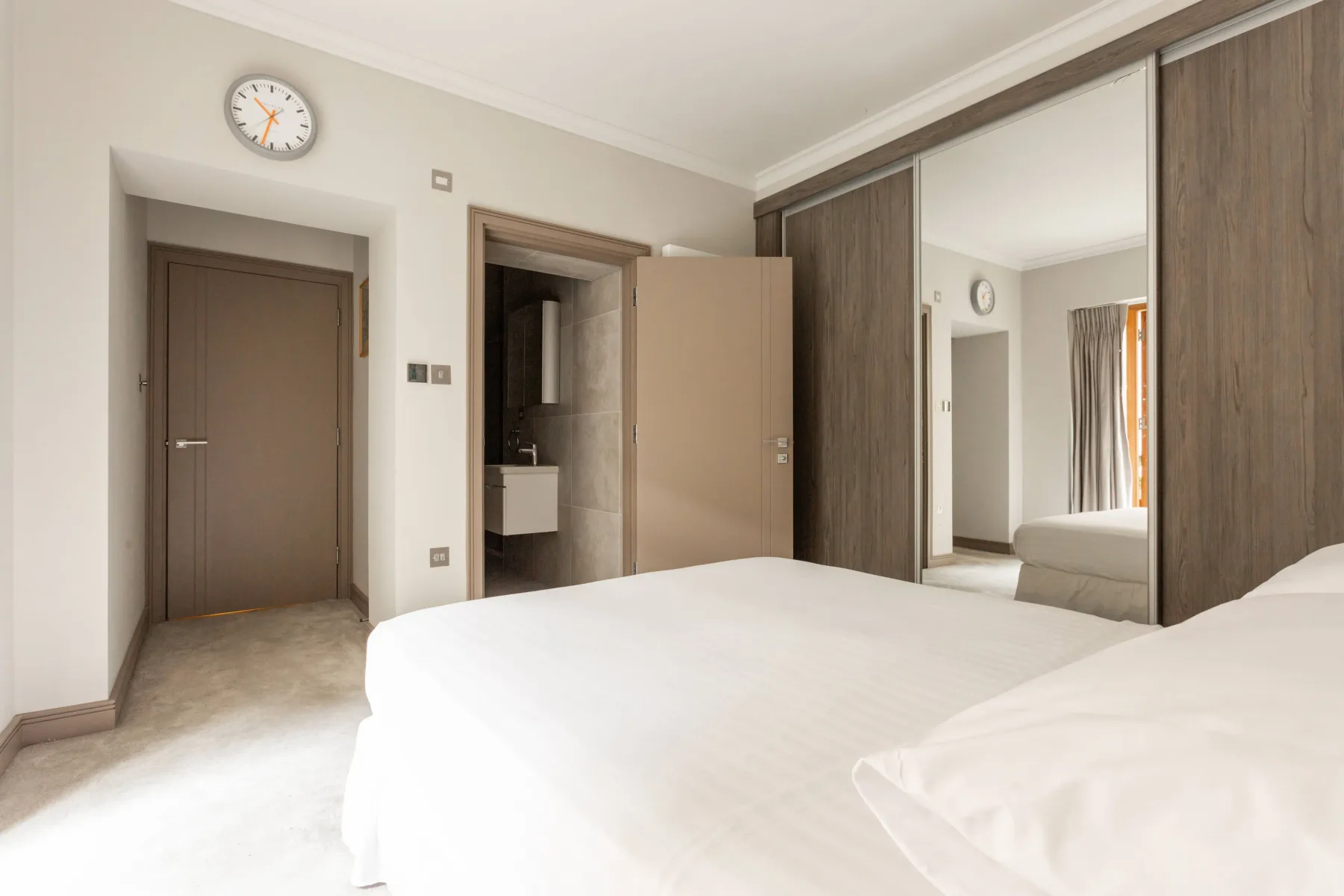 A bedroom with a white bed and mirrored wardrobe.