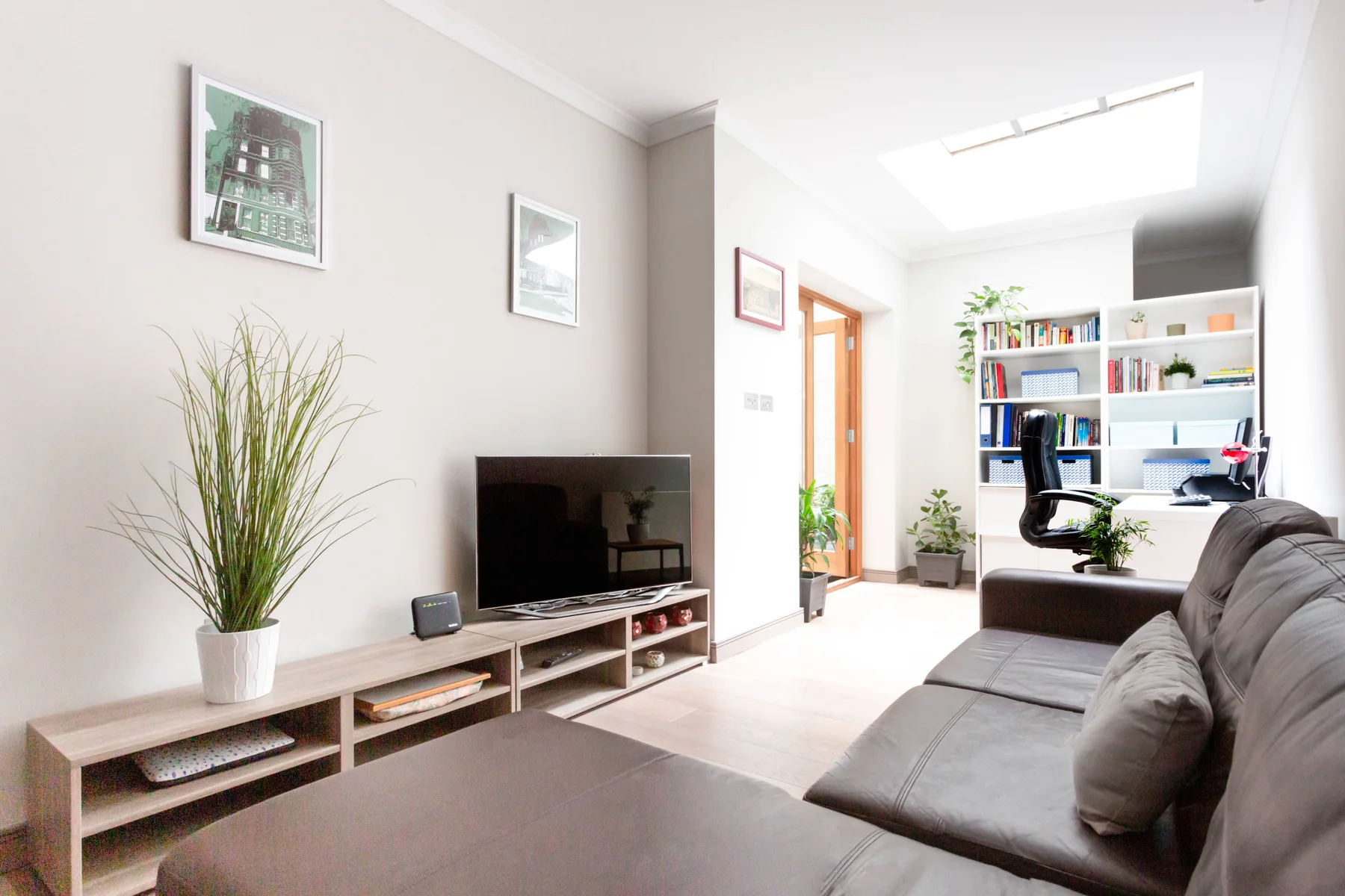 A bright living room with a sectional sofa, television, and desk area.