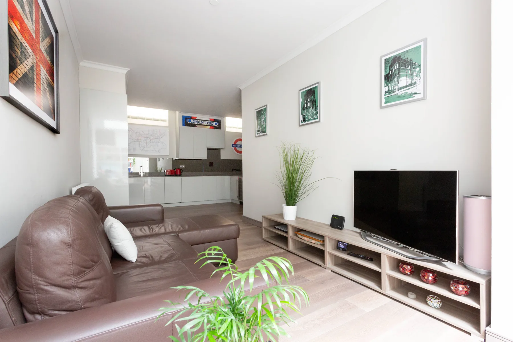 A living room with brown seating, a television, and a view into the kitchen.