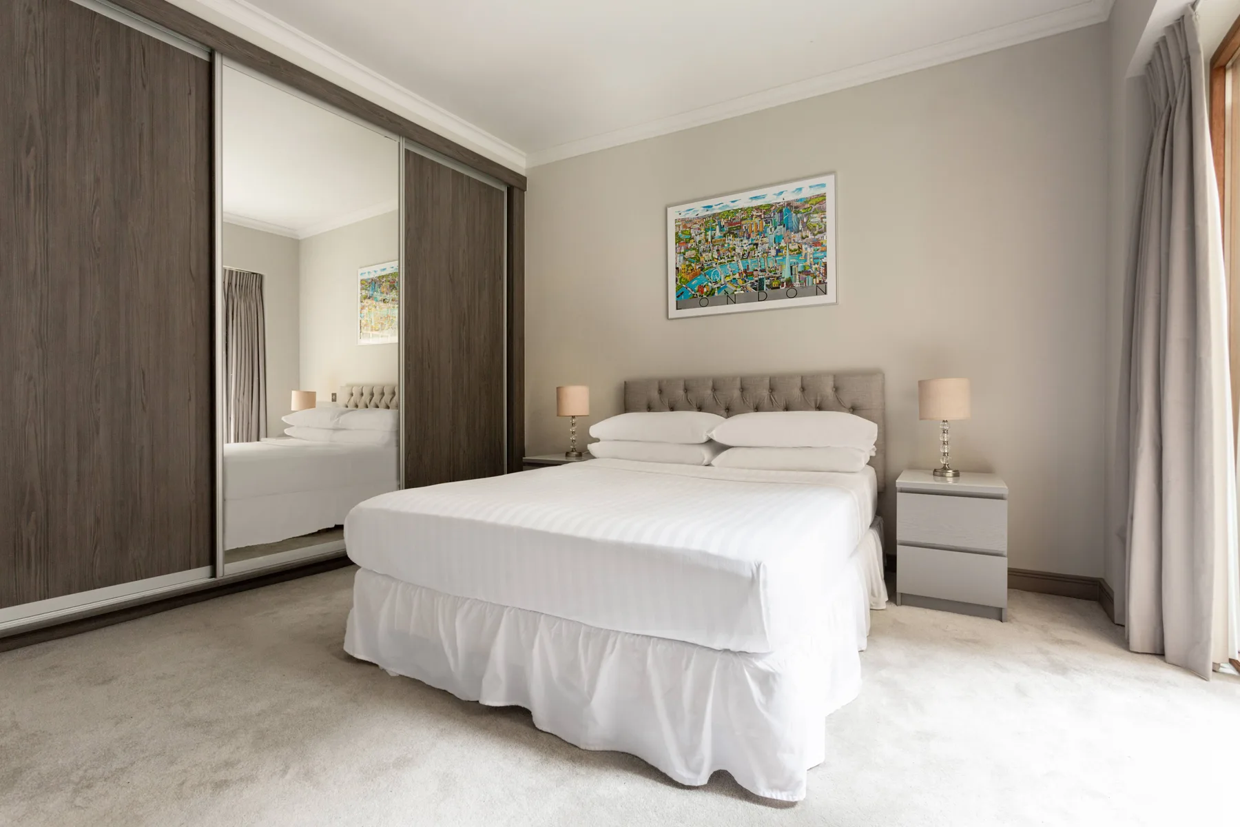 A bedroom with a neatly made bed, bedside tables, and a mirrored wardrobe.