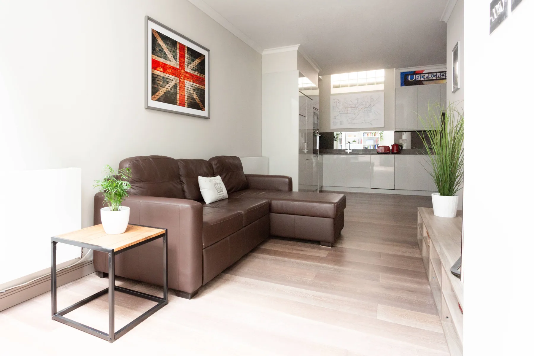 A living room with brown seating and a small side table, with a kitchen beyond.