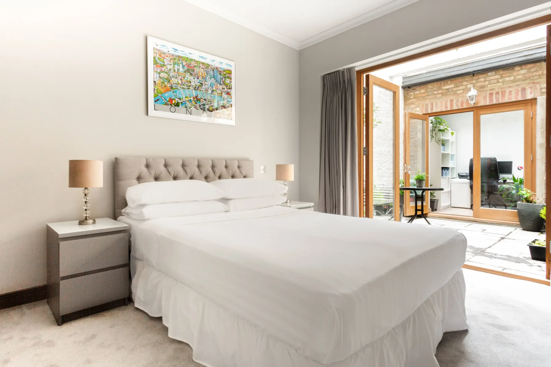 A bedroom with a neatly made bed beside open doors to a bright patio.
