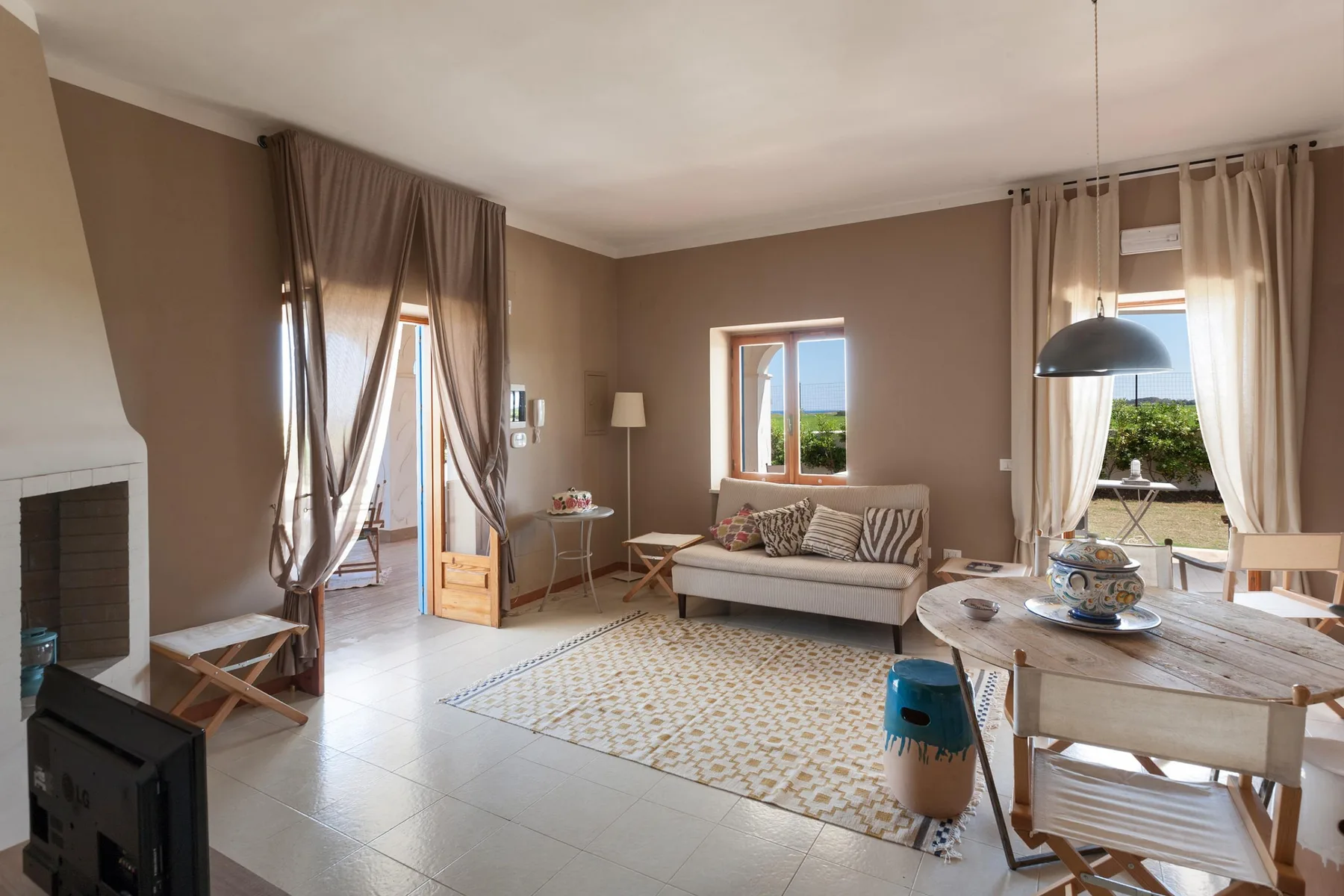 Una sala luminosa con sofá, mesa de comedor y ventanas con vistas a la vegetación.
