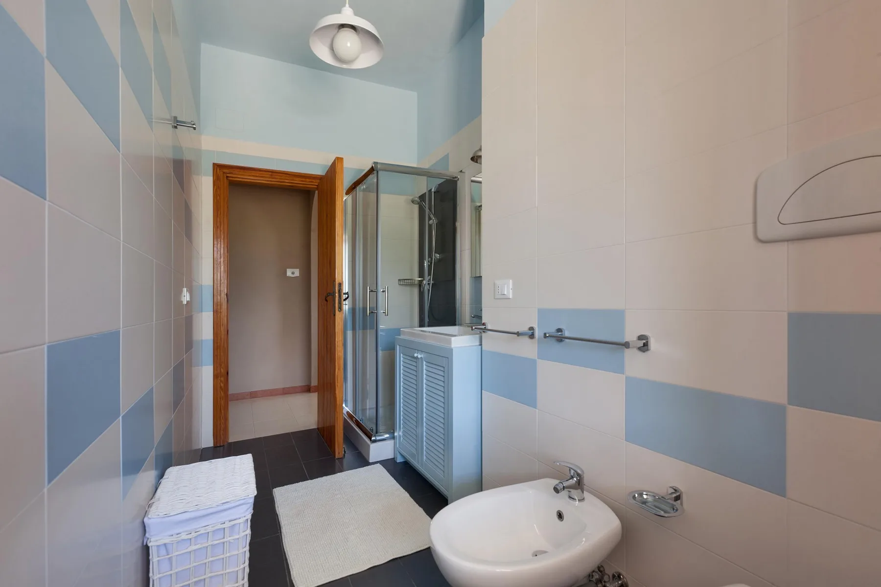 Un baño con azulejos, un lavabo, una cesta de toallas y una ducha.
