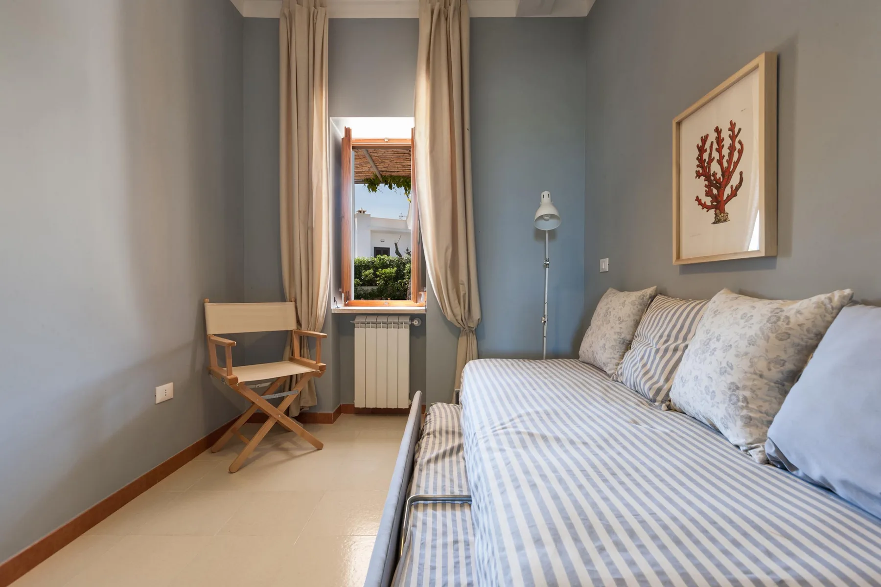 Un dormitorio con una cama a rayas, una ventana y una silla de madera.