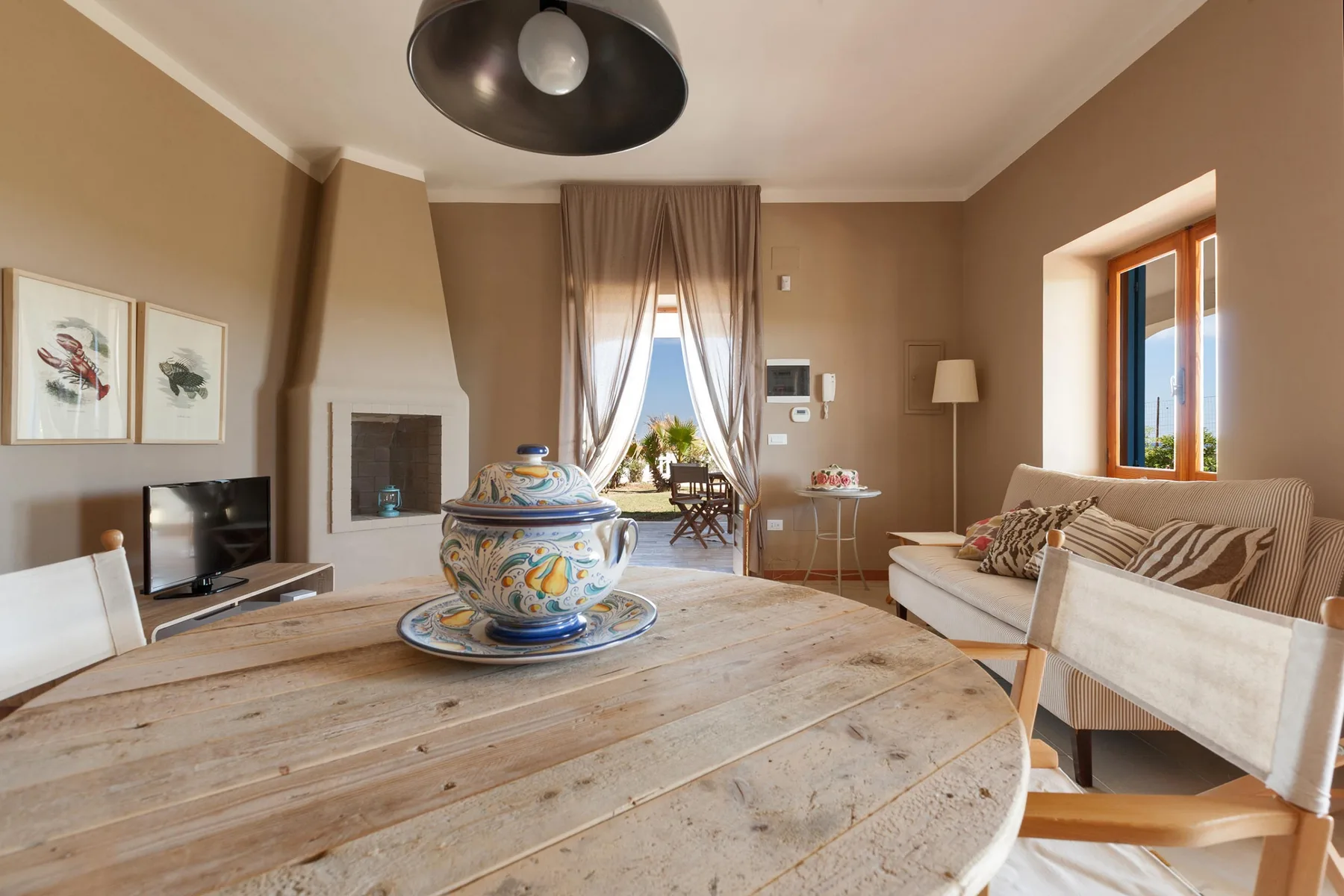 A warm-toned living room with a wooden table and seating around a fireplace.