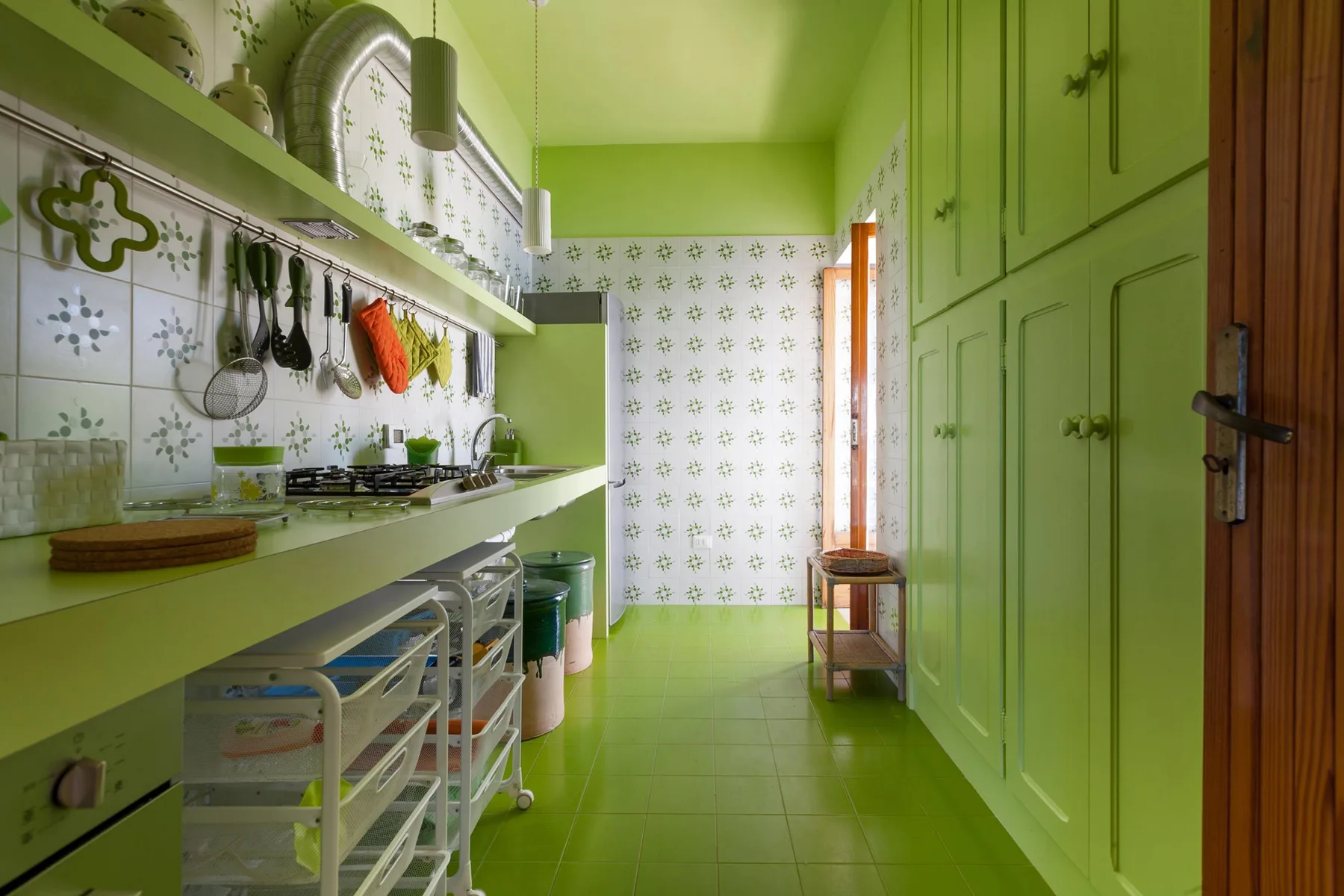 Una cocina verde luminosa con una encimera larga, utensilios de cocina y armarios.