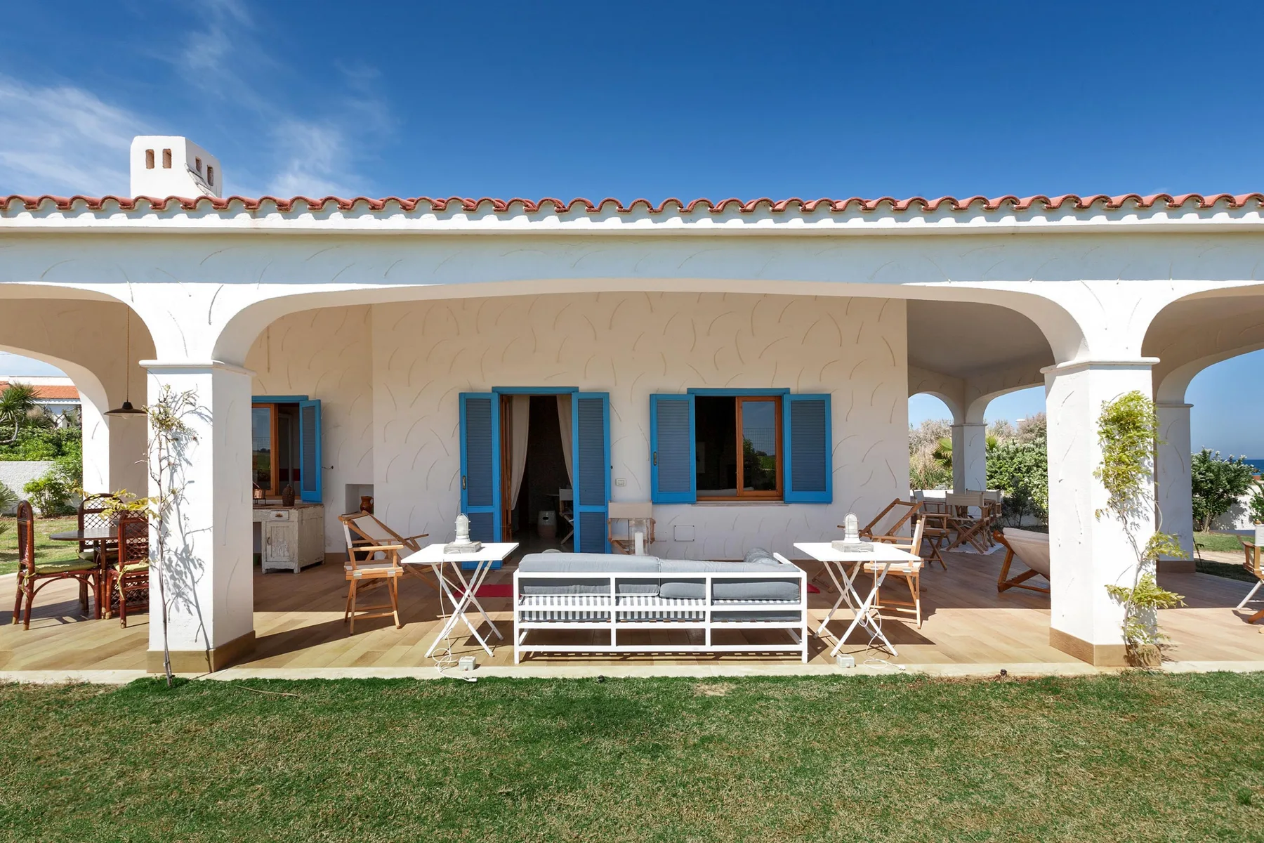 Un patio exterior cubierto con asientos y ventanas con marcos azules.