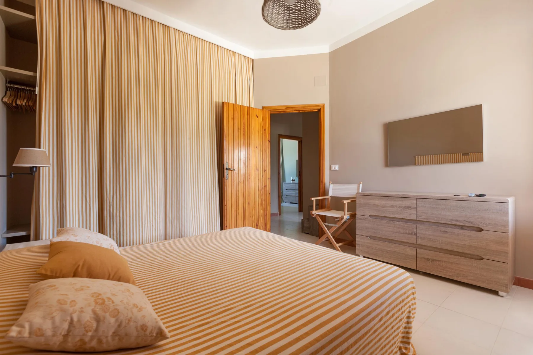 A bedroom with a striped bed, full-length curtains, and a wooden dresser.